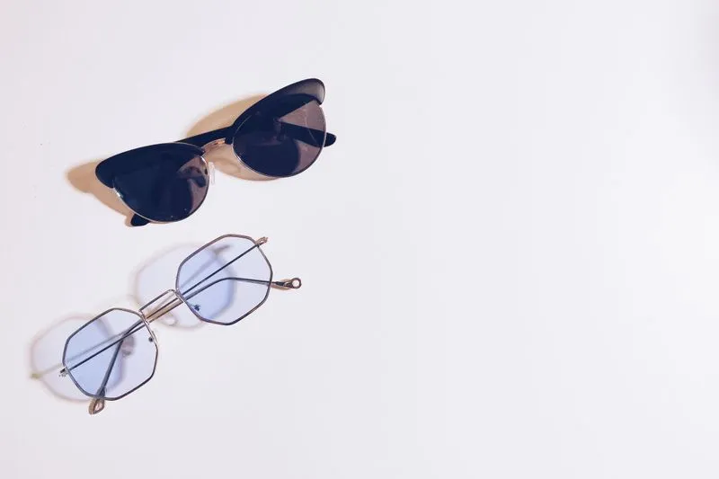 Deux paires de lunettes aux verres plus ou moins foncés, posées sur une surface blanche
