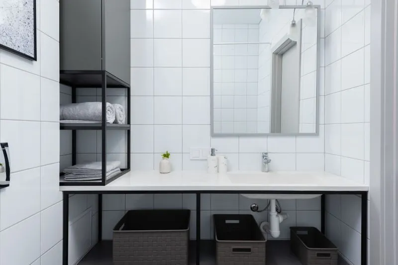 Étagère murale noire avec des serviettes pliées, à côté d'un plan vasque et de paniers de rangement