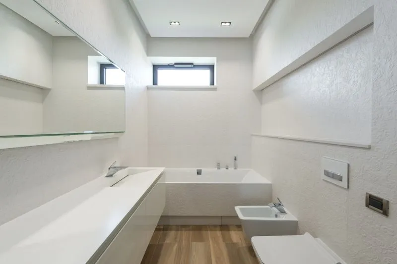 Salle de bains aux murs blancs du sol au plafond, avec une petite fenêtre, une baignoire et un lavabo