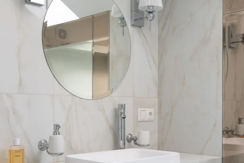 Petite salle de bains lumineuse aux murs clairs, avec un grand miroir rond au-dessus de la vasque