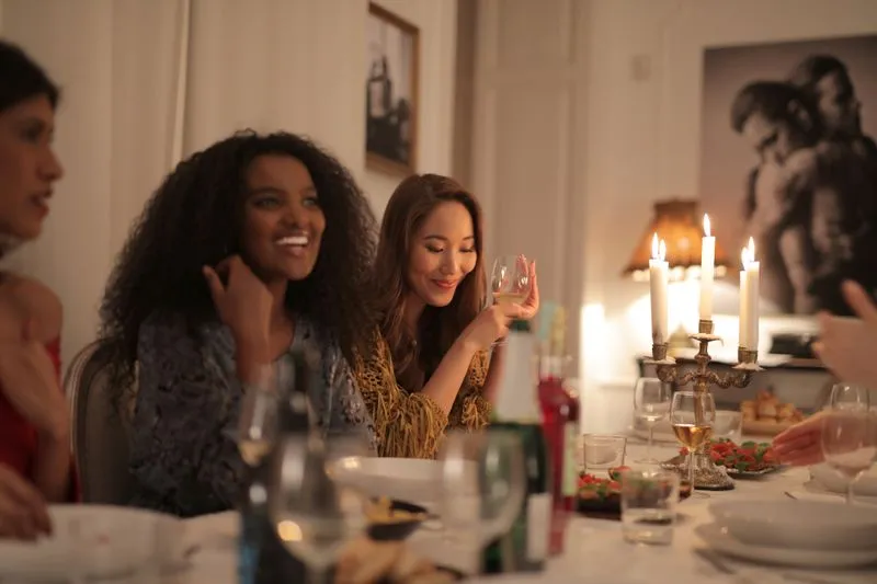 Amies attablées pour un dîner aux chandelles, l'une un verre de vin à la main, en train de rire