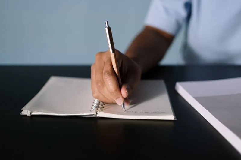 Main qui écrit au stylo dans un carnet à spirale ouvert