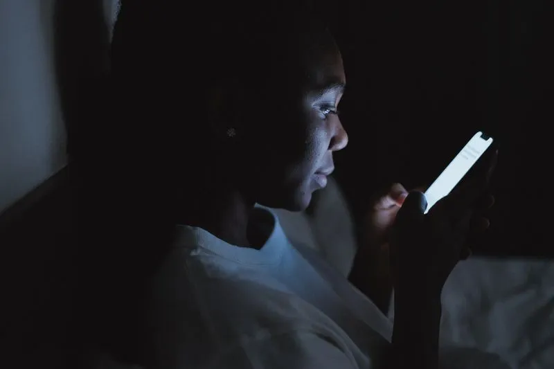 Jeune femme assise dans le noir le soir, le visage éclairé par l'écran de son téléphone
