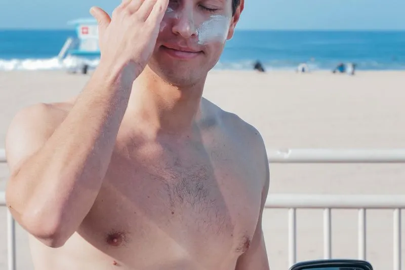 Homme en extérieur qui étale de la crème solaire sur son visage, une trace blanche sur la joue
