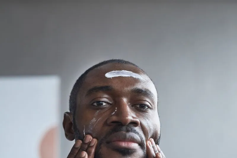 Homme face à l'objectif, une trace de crème blanche sur le front, les deux mains posées sur les joues
