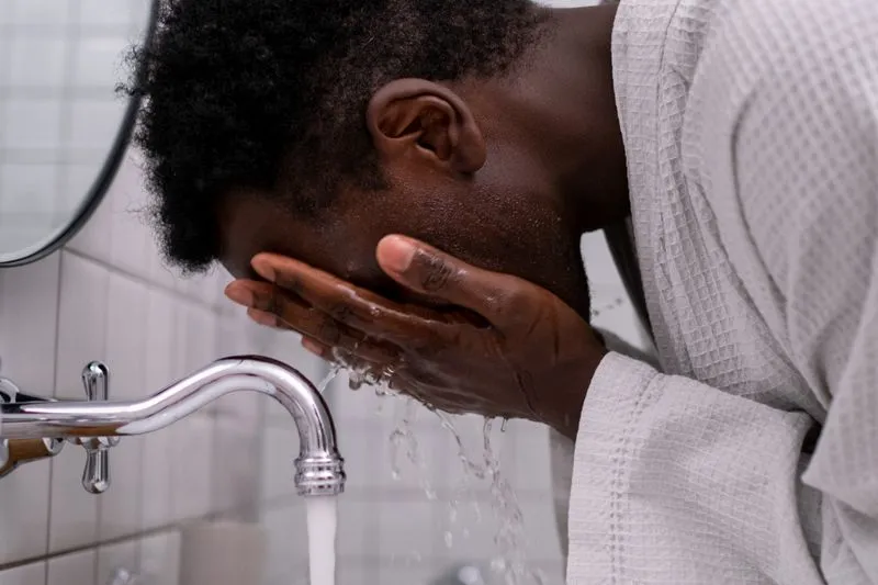 Homme penché au-dessus d'un lavabo qui se rince le visage à deux mains avec de l'eau
