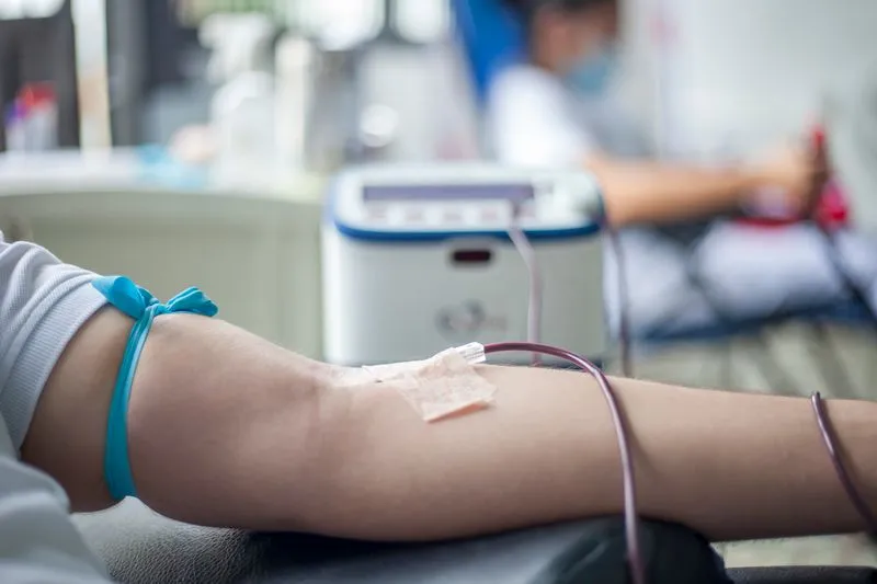 Bras tendu relié par un tube à un appareil de prélèvement, un autre donneur installé en arrière-plan