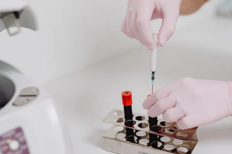 Technicienne de laboratoire en blouse manipulant des tubes d'échantillons sanguins sur un portoir