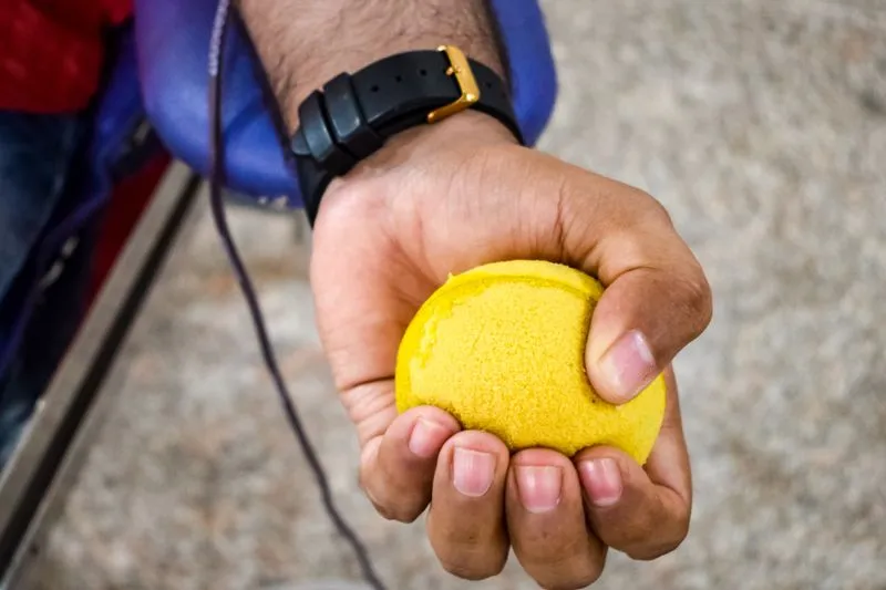 Main d'un donneur serrant une balle en mousse jaune pendant un don de sang, un tube le long de l'avant-bras