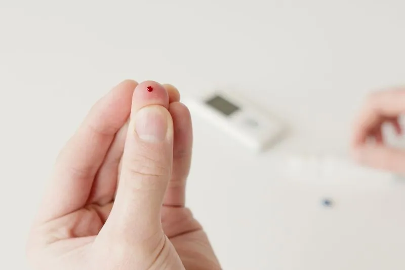 Gros plan sur un doigt piqué dont on recueille une goutte de sang pour un test rapide