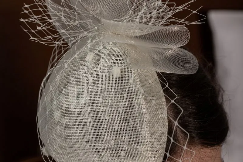 Coiffe en sisal blanc et voilette résille, posée de côté sur des cheveux bruns