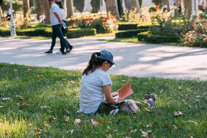 Jeune femme assise dans l'herbe d'un parc en train de lire un livre, au soleil