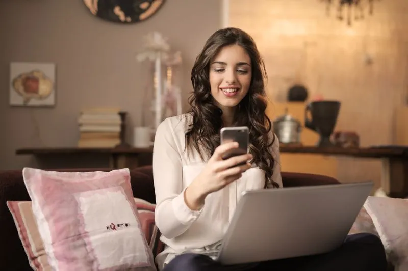 Jeune femme assise sur un canapé qui fait défiler des annonces sur son téléphone