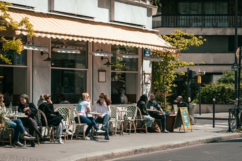 Terrasse de café parisienne en été, tables de bistrot alignées sur le trottoir et passants