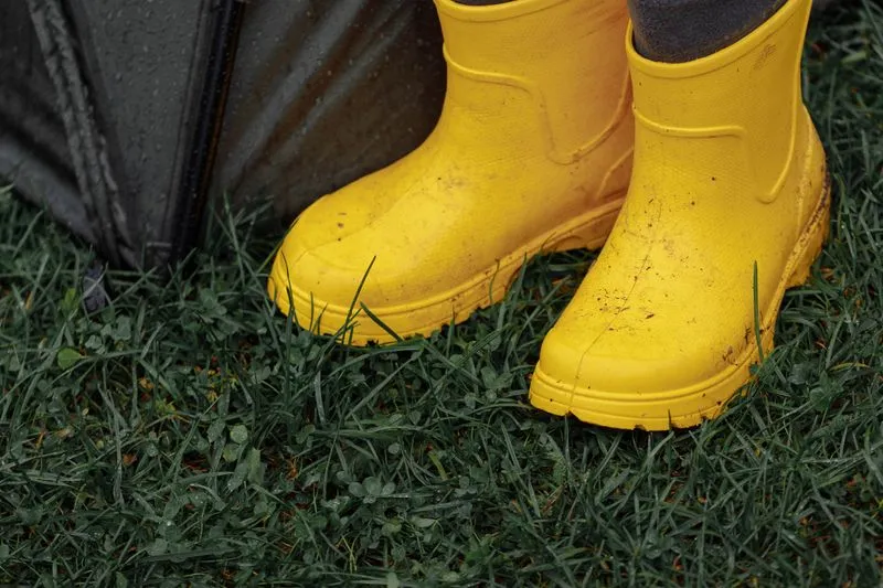 Bottes de pluie jaunes portées dans l'herbe humide, à côté d'un parapluie fermé, après une averse de festival