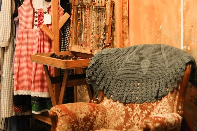 Portant de vêtements et bijoux de seconde main dans une boutique vintage, avec une robe à carreaux et des lunettes de soleil en vitrine