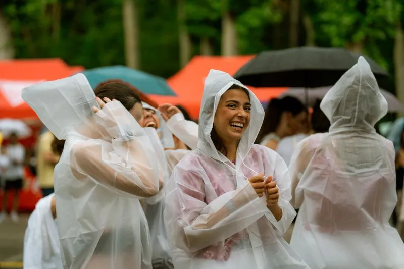 Groupe de festivaliers riant sous des ponchos de pluie transparents, devant des tentes colorées, sous l'averse