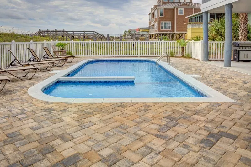 Piscine avec terrasse et transats, bordée au loin par une clôture blanche de jardin