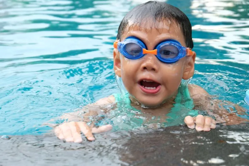 Jeune enfant portant des lunettes de piscine, s'appuyant au bord du bassin en nageant