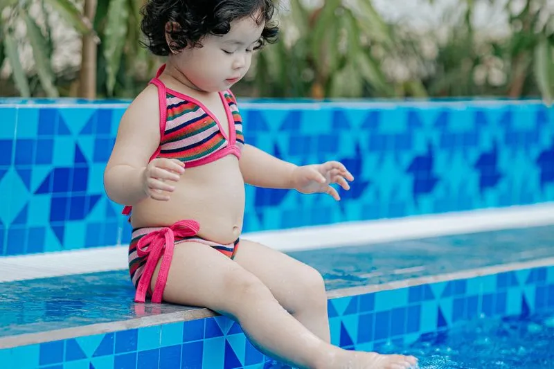 Jeune enfant assis au bord d'une piscine enterrée, les pieds dans l'eau