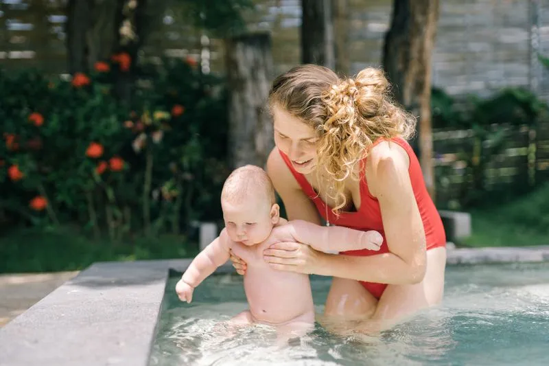 Mère dans l'eau d'une piscine tenant son bébé sous les bras