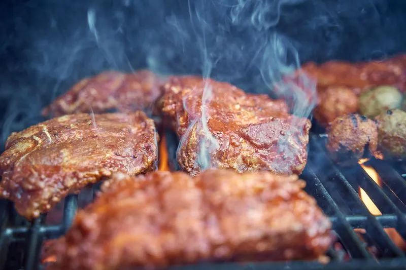 Gros plan sur des morceaux de viande bien colorés et fumants sur la grille d'un barbecue, avec des flammes visibles en dessous