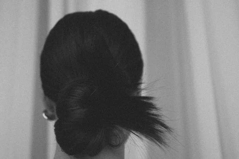 Vue de dos d'un chignon bas légèrement torsadé, en noir et blanc, avec quelques mèches folles à la base