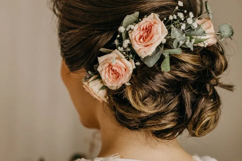 Vue de dos d'un chignon bas et souple orné de roses, dans une lumière chaude