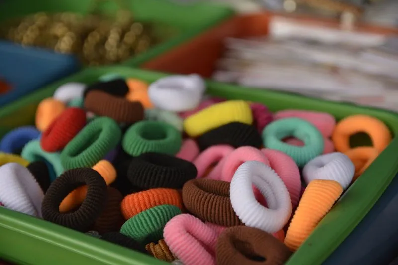 Des dizaines d'élastiques à cheveux recouverts de tissu, de toutes les couleurs, dans un bac vert