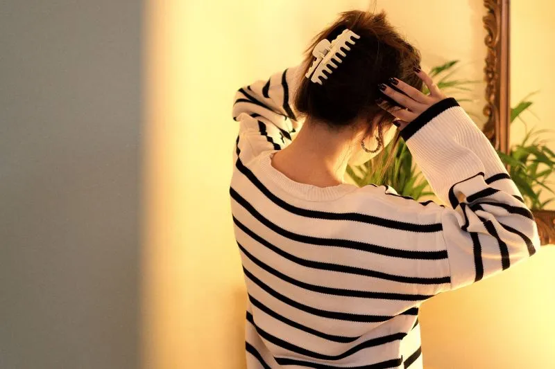 Vue de dos d'une femme en pull rayé qui referme une pince crabe blanche sur ses cheveux relevés
