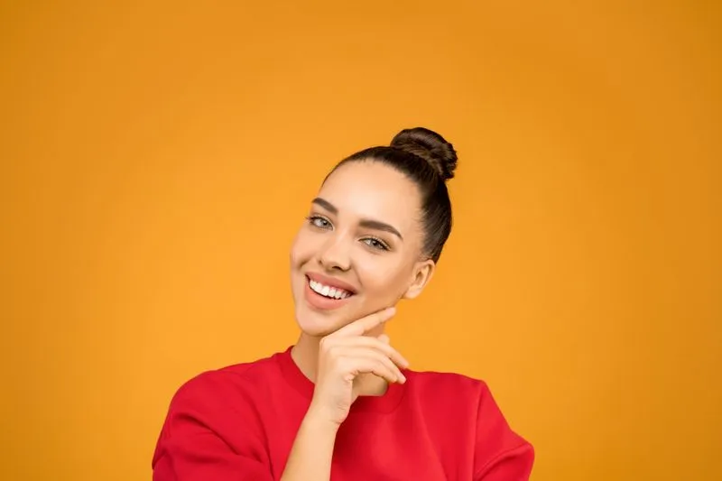 Jeune femme souriante, cheveux ramenés en chignon haut et lisse, sur fond orangé