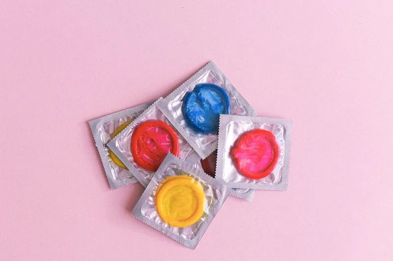 Des préservatifs dans leurs emballages de couleurs vives, éparpillés sur un fond rose clair