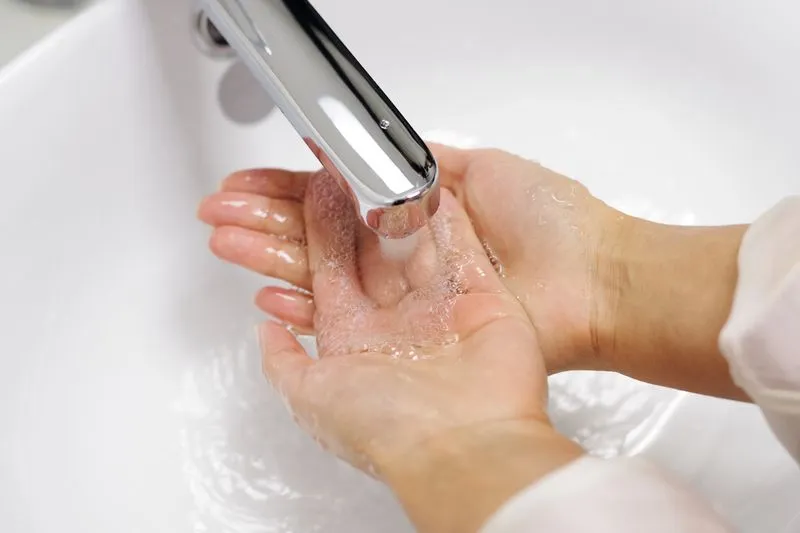 Des mains savonnées sous le filet d'eau d'un robinet, au-dessus d'un lavabo blanc