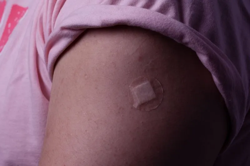 Un petit pansement carré au centre d'un rond adhésif, posé sur le haut du bras d'une jeune femme après une injection