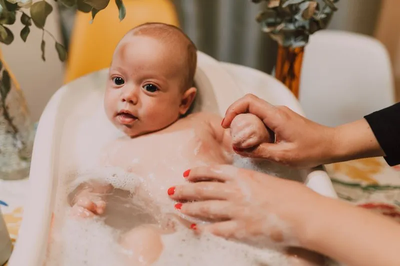 Bébé assis dans une petite baignoire d'eau tiède, tenu par la main d'un adulte