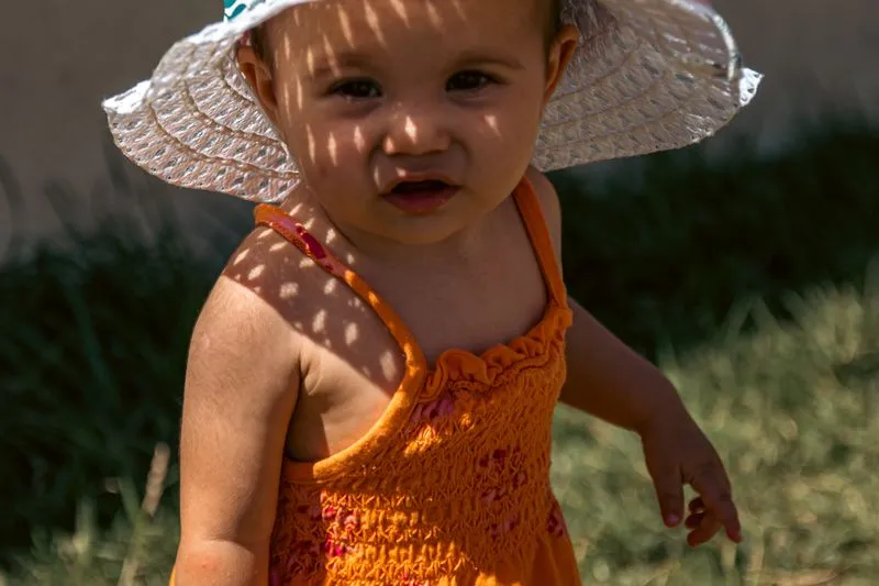 Bébé coiffé d'un chapeau de soleil à larges bords, motifs d'ombre et de lumière sur le visage