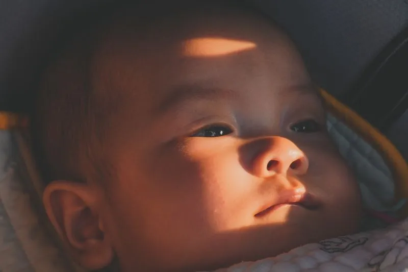 Visage de bébé installé dans un siège auto, traversé par un rayon de soleil direct