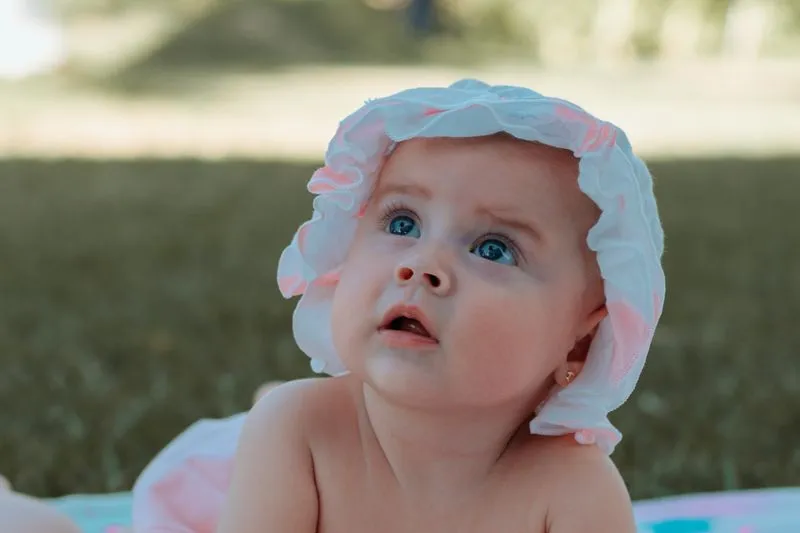 Bébé coiffé d'un bonnet à volants, allongé sur une couverture colorée en extérieur