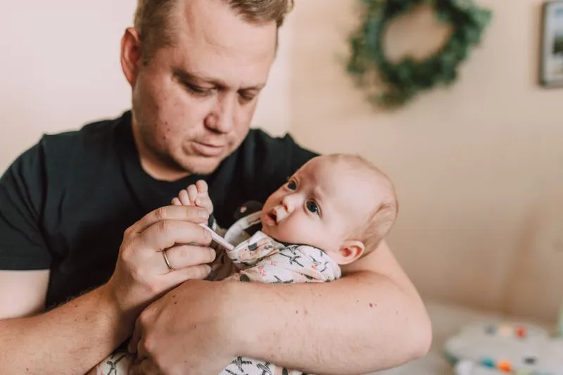 Père qui tient son bébé dans les bras et lui prend la température avec un thermomètre, à la maison