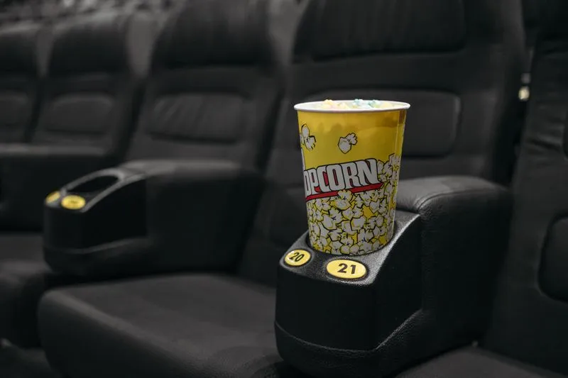 Gros plan sur un pot de pop-corn jaune posé dans le porte-gobelet d'un fauteuil de cinéma