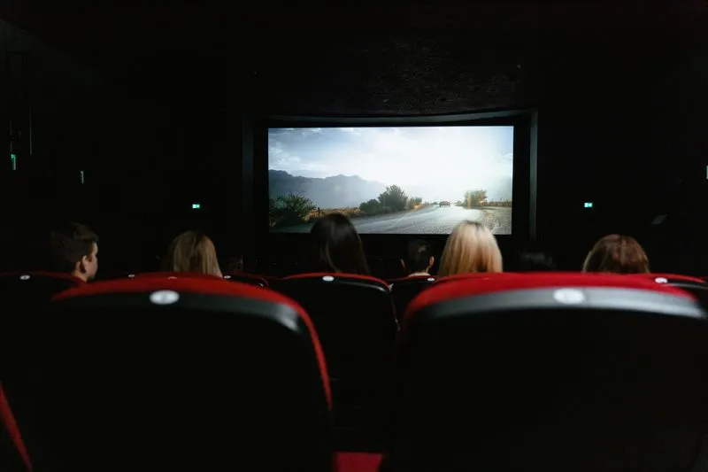 Salle de cinéma aux fauteuils rouges, spectateurs de dos face à l'écran lumineux