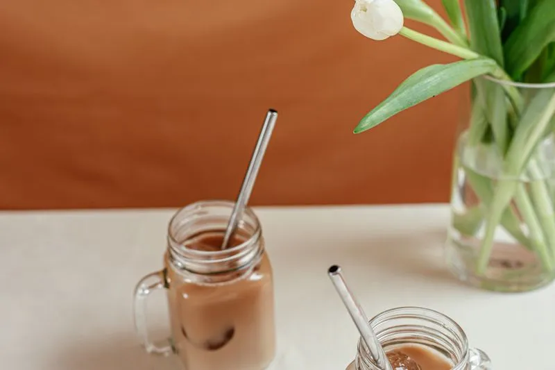 Deux verres de café glacé avec pailles en inox, posés sur une table près d'un vase de tulipes