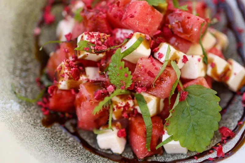 Une assiette de dés de pastèque et de feta, parsemée de menthe fraîche et nappée d'un filet de balsamique