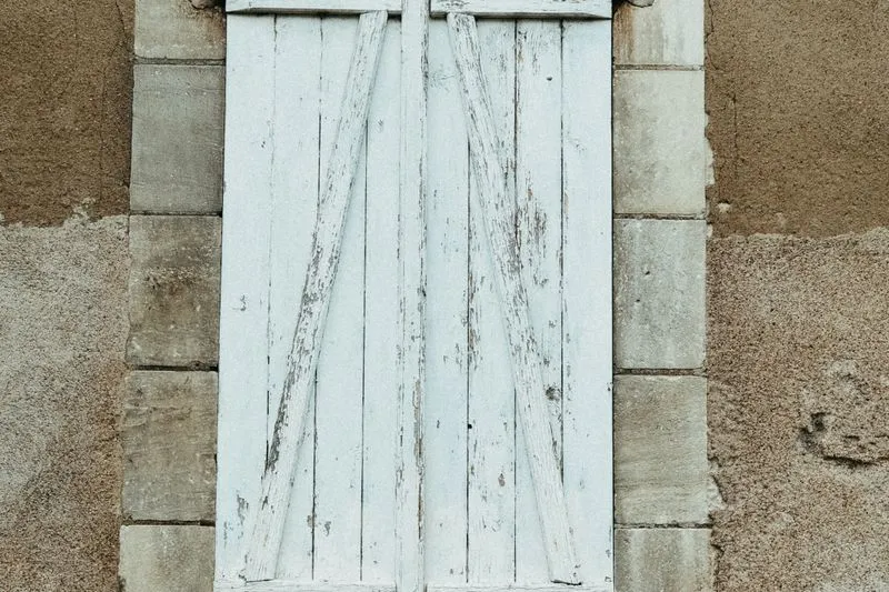 Volet en bois peint en blanc, fermé, sur la façade en pierre d'une maison ancienne