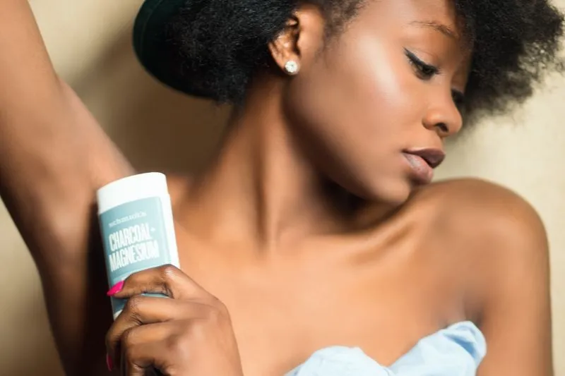 Jeune femme appliquant un déodorant stick sous le bras, en gros plan