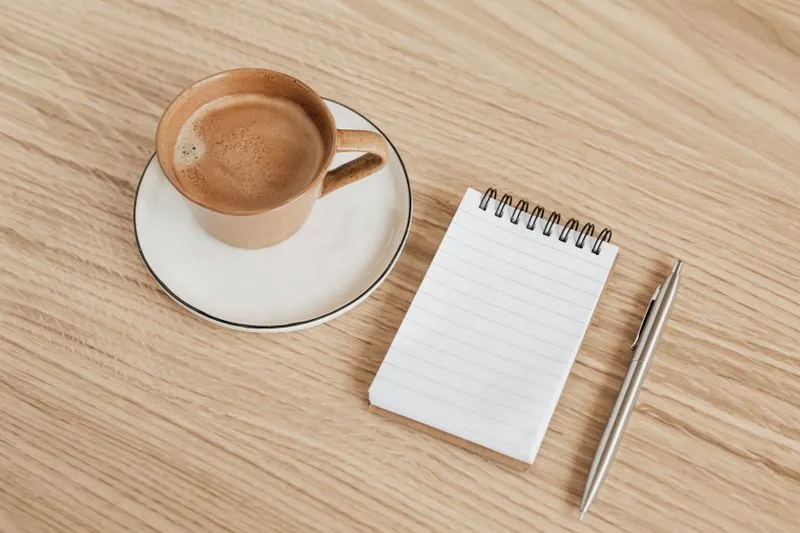 Carnet ouvert et stylo posés sur une table en bois, à côté d'une tasse de café