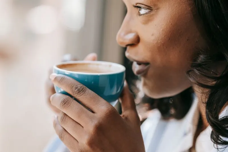 Gros plan sur une jeune femme qui boit dans une tasse, le regard tourné vers la lumière d'une fenêtre