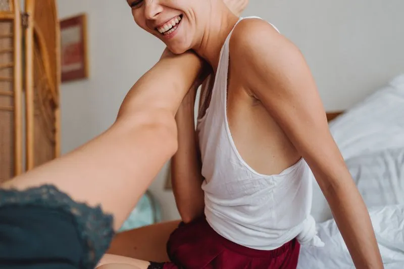 Couple qui rit sur un lit, une jambe levée jusqu'à l'épaule dans un fou rire complice