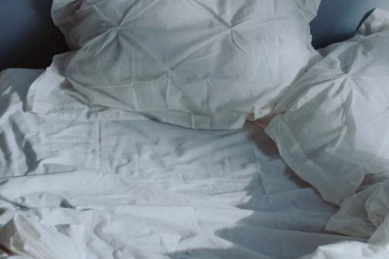 Oreillers capitonnés et draps froissés sur un lit, dans une lumière douce