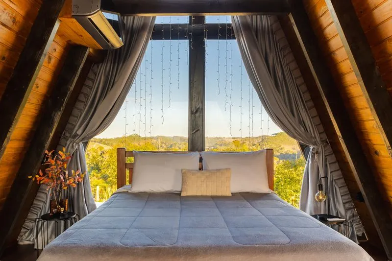 Chambre de location de vacances avec une grande baie vitrée habillée de rideaux, vue sur la campagne à la tombée du jour